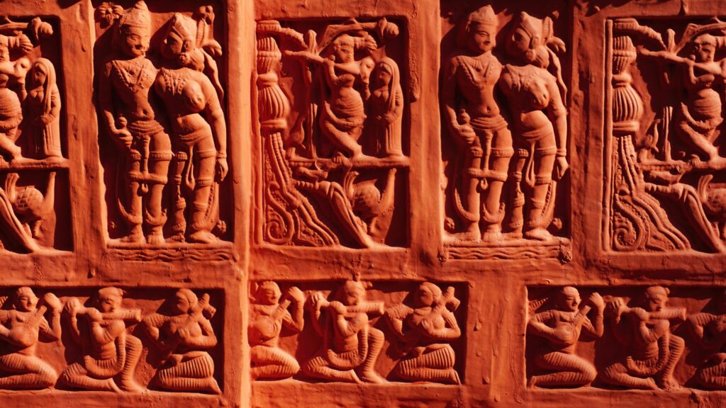 Detailed stone carvings depicting historical and cultural figures from ancient times at a temple wall.