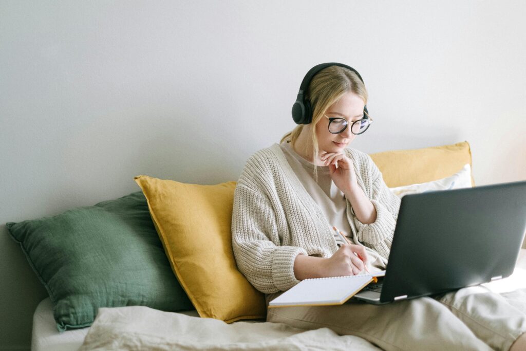 pexels-photo-4458554-4458554 A focused woman in glasses and headphones works on a laptop from a cozy bed.